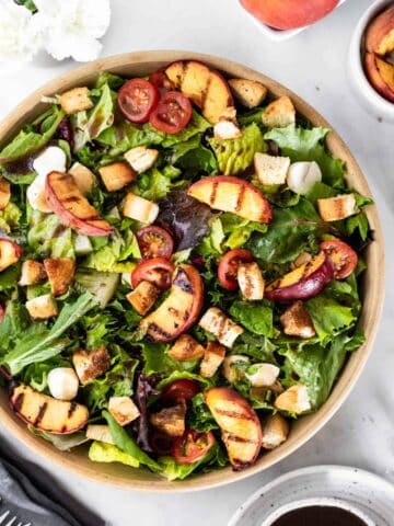 Bruschetta salad in a large bowl topped with grilled peaches, mozzarella, croutons, and sliced tomatoes.