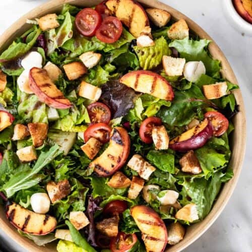 Bruschetta salad in a large bowl topped with grilled peaches, mozzarella, croutons, and sliced tomatoes.