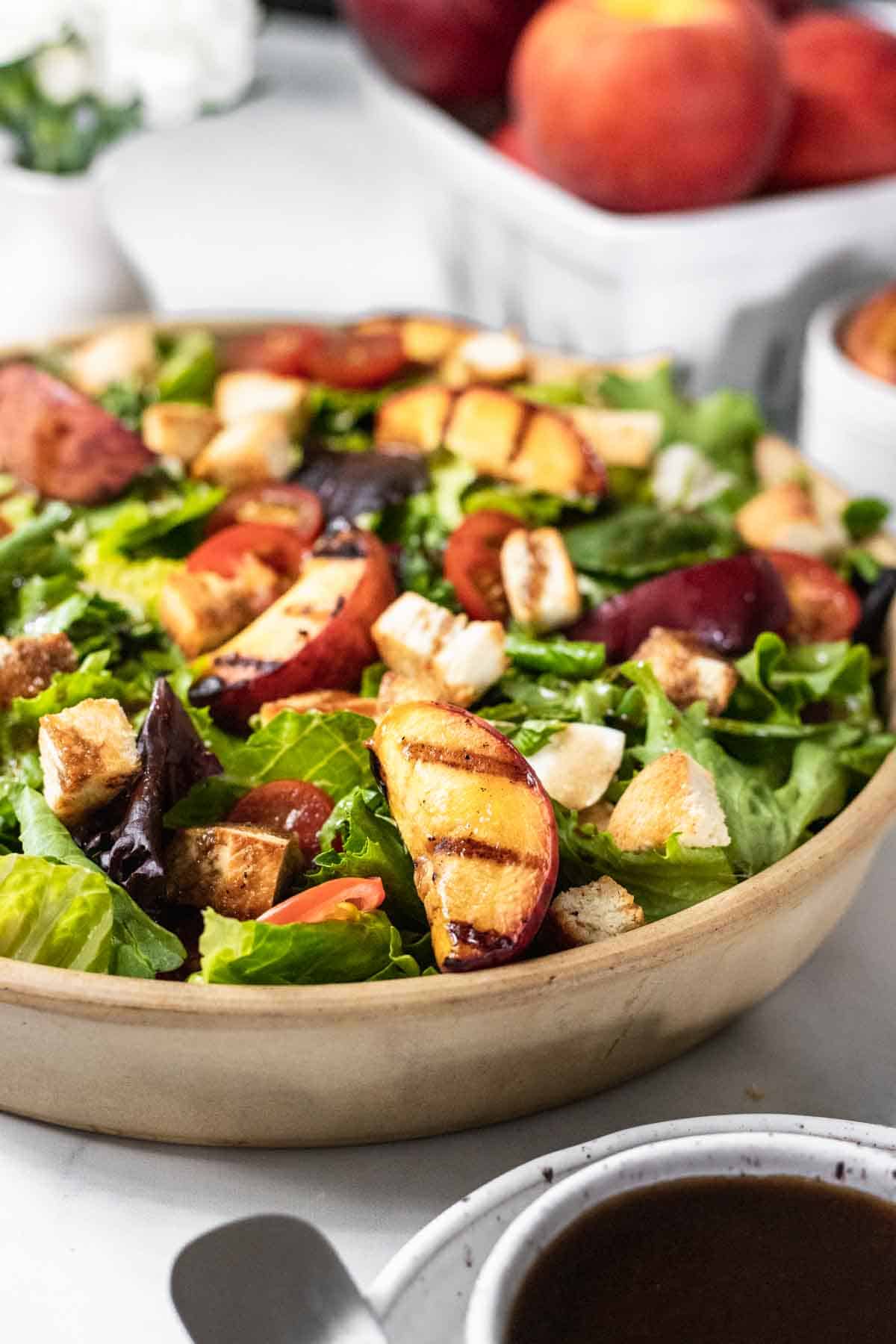 Bruschetta salad in a bowl with grilled peaches and whole fresh peaches in a basket behind it.