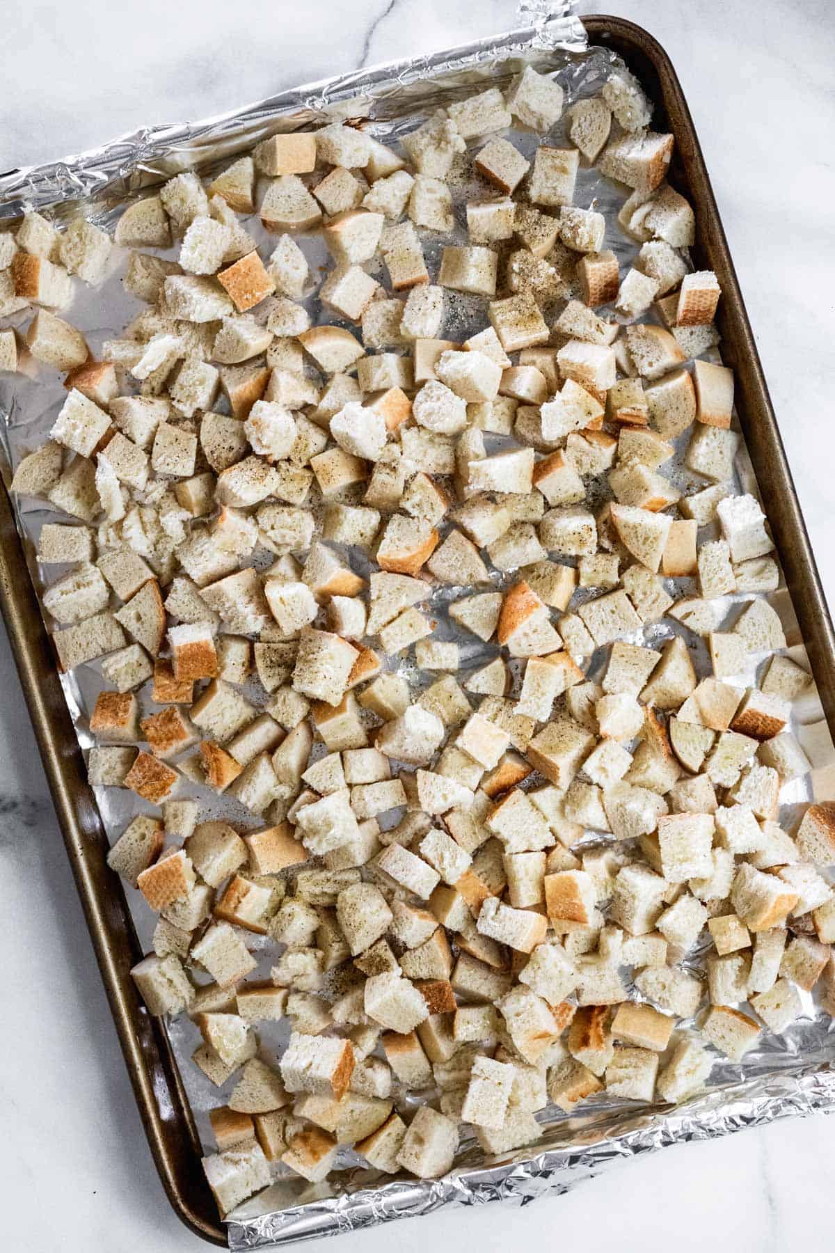 Diced and seasoned baguette on a sheet pan.