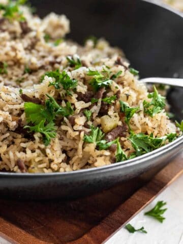 Dirty rice garnished with parsley in a black bowl.