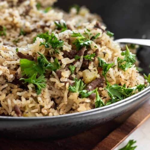 Dirty rice garnished with parsley in a black bowl.