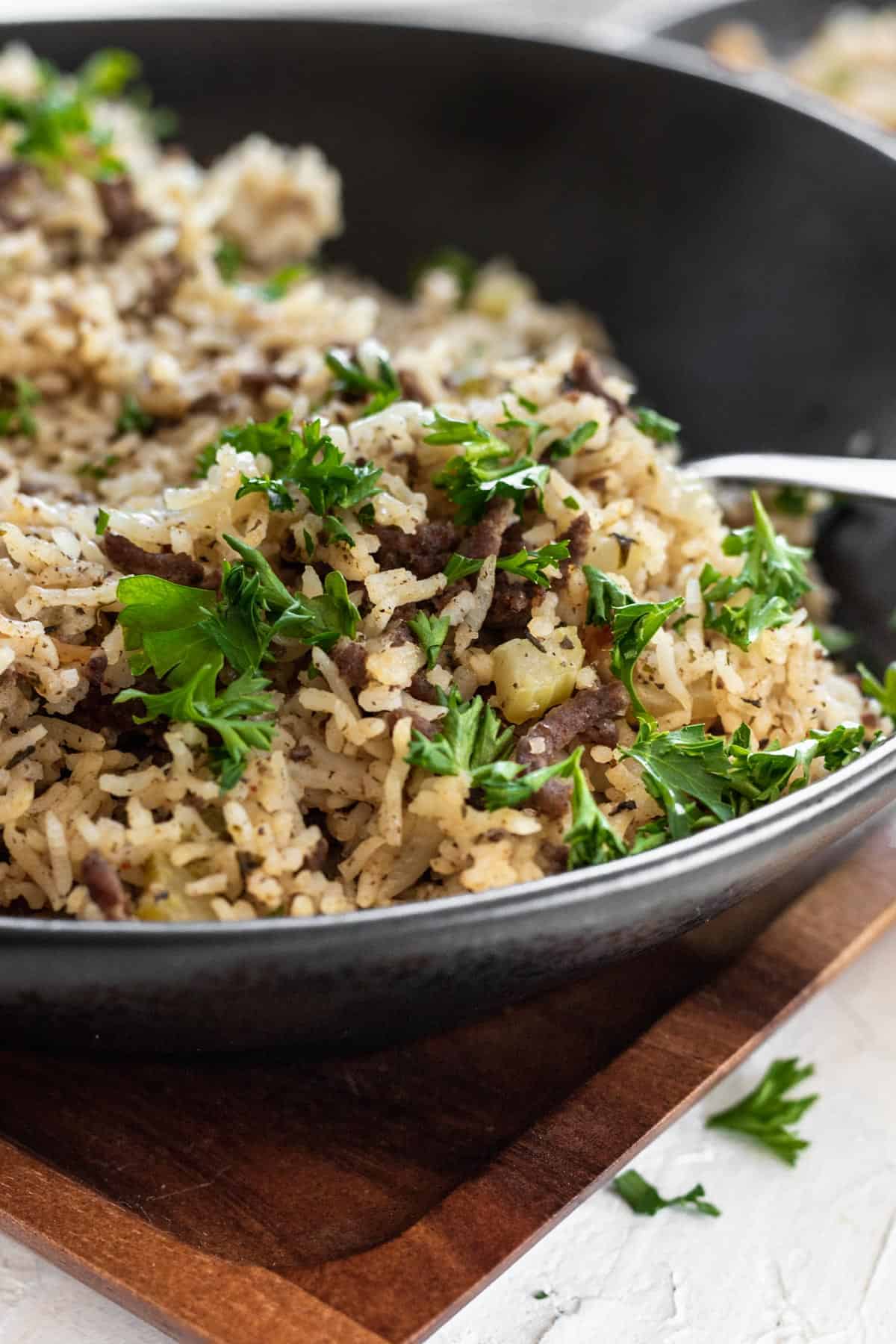 Dirty rice garnished with parsley in a black bowl.