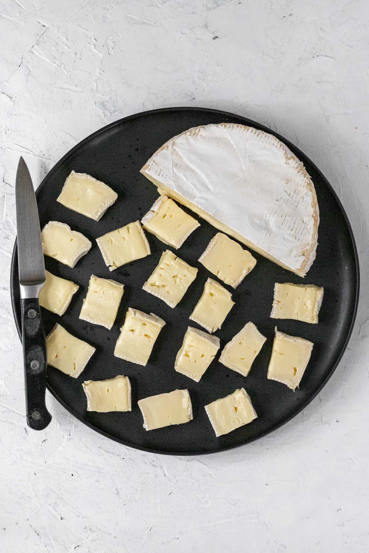 Cubed brie on a plate with a knife.