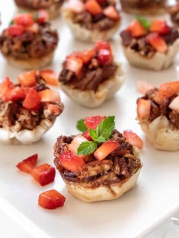 A closeup side view of the bacon bourbon pecan brie bites topped with diced strawberries and a garnish of fresh mint.