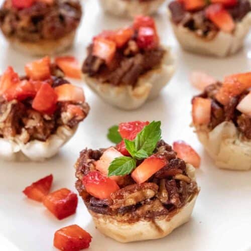 A closeup side view of the bacon bourbon pecan brie bites topped with diced strawberries and a garnish of fresh mint.