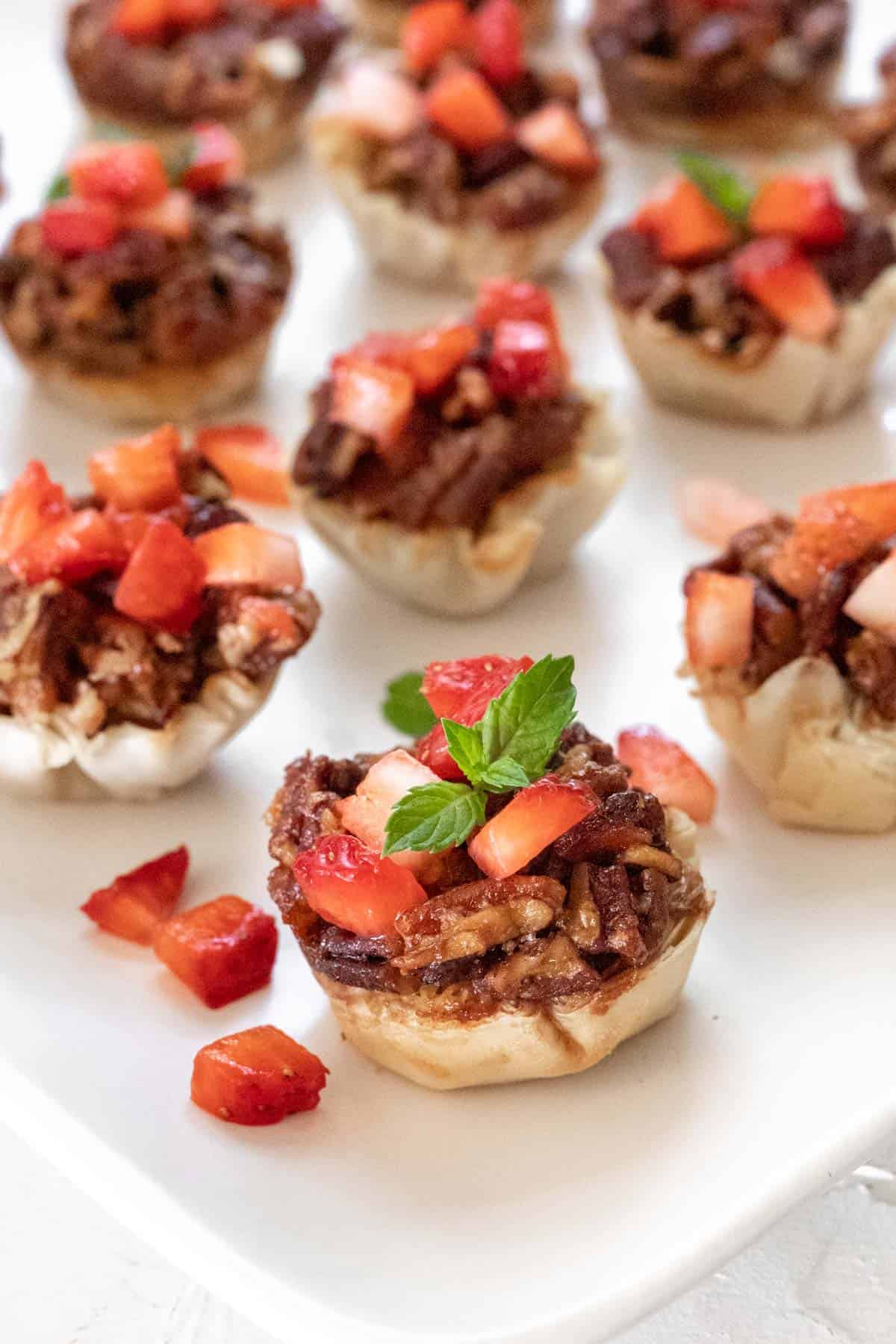 A closeup side view of the bacon bourbon pecan brie bites topped with diced strawberries and a garnish of fresh mint.