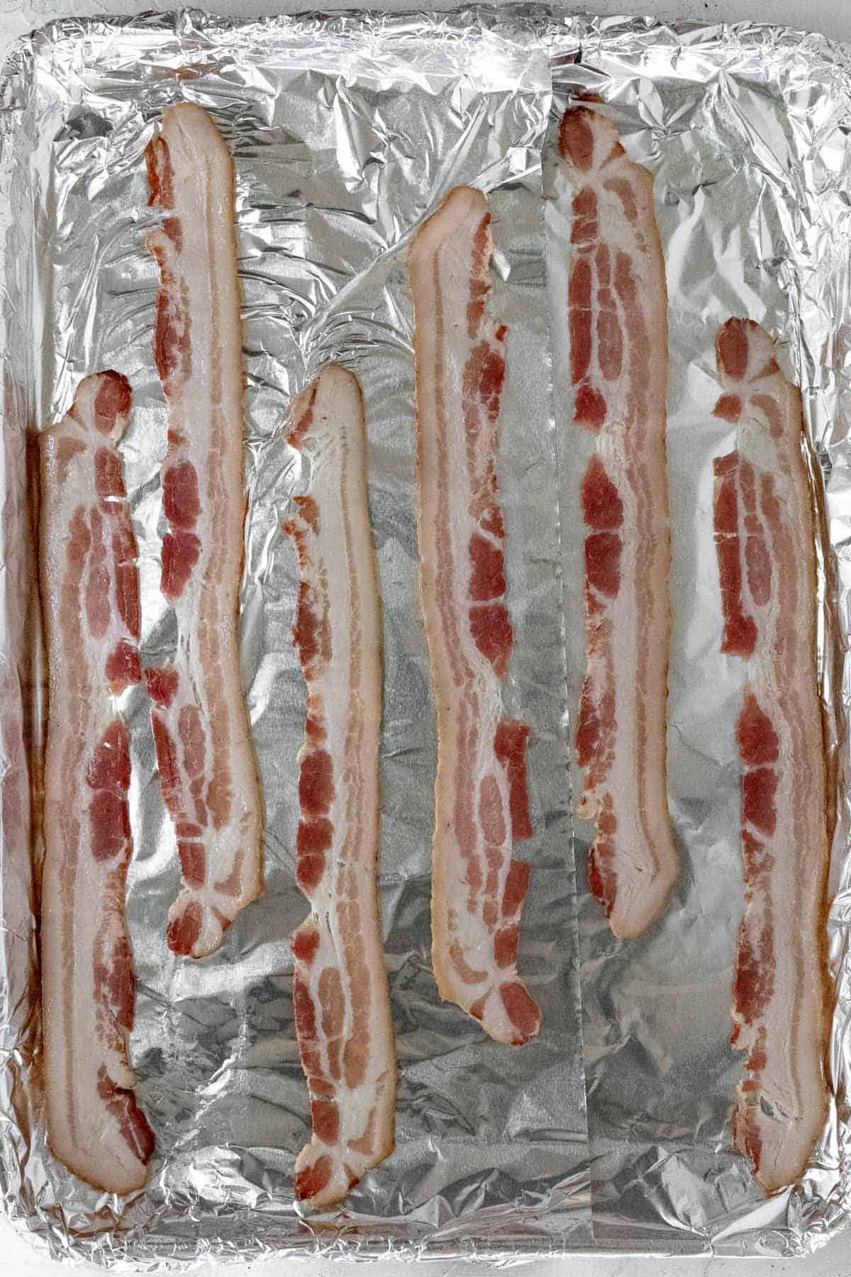 Strips of bacon on a sheet pan before going in the oven.
