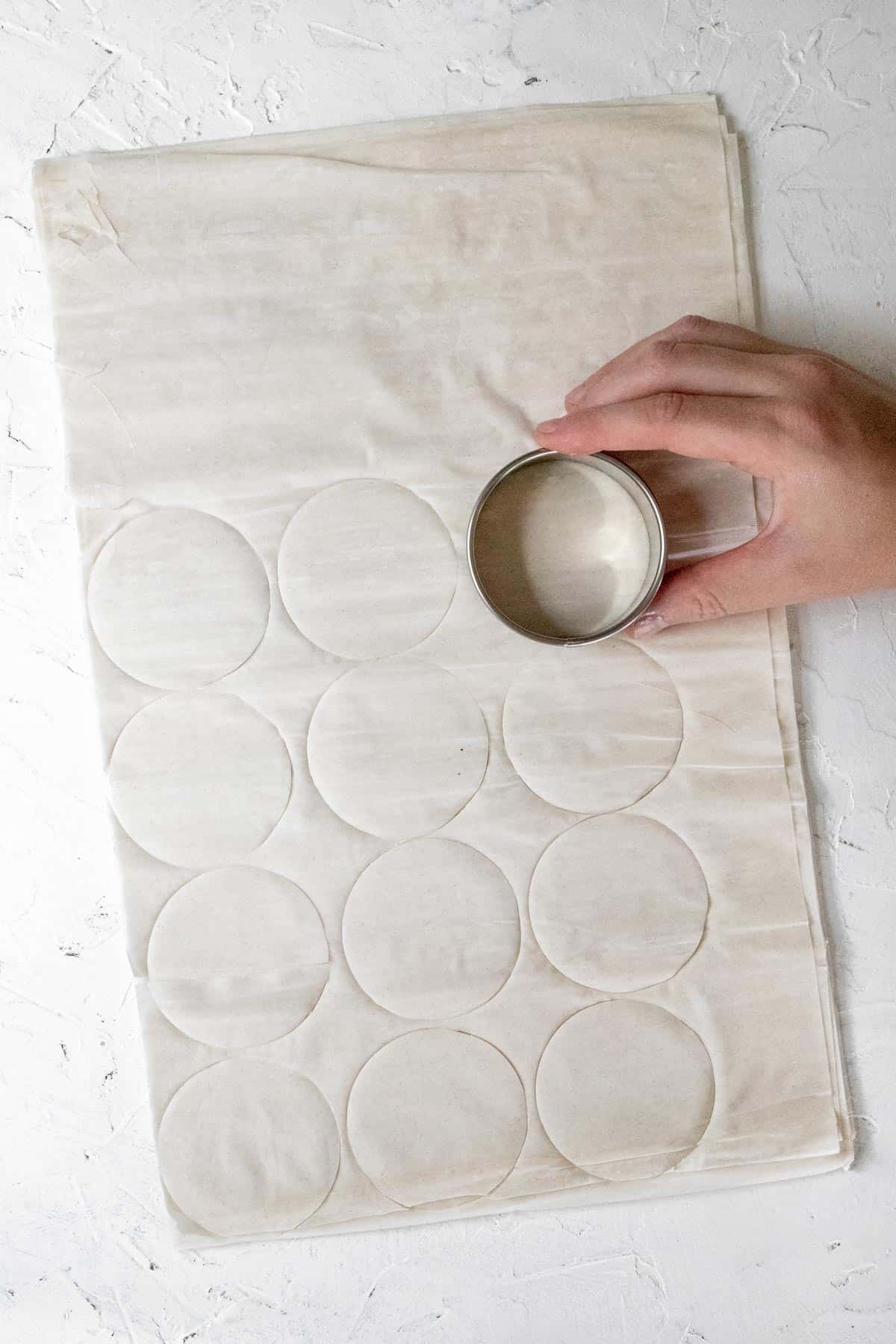 A hand with a circular cookie cutter cutting circles of phyllo dough.