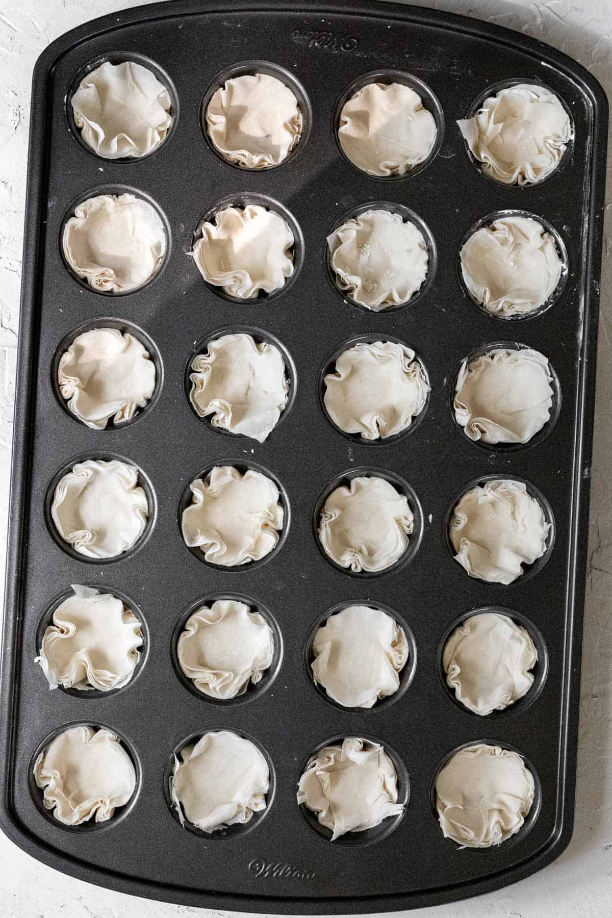 Raw phyllo dough pressed into each slot in a mini muffin tin.