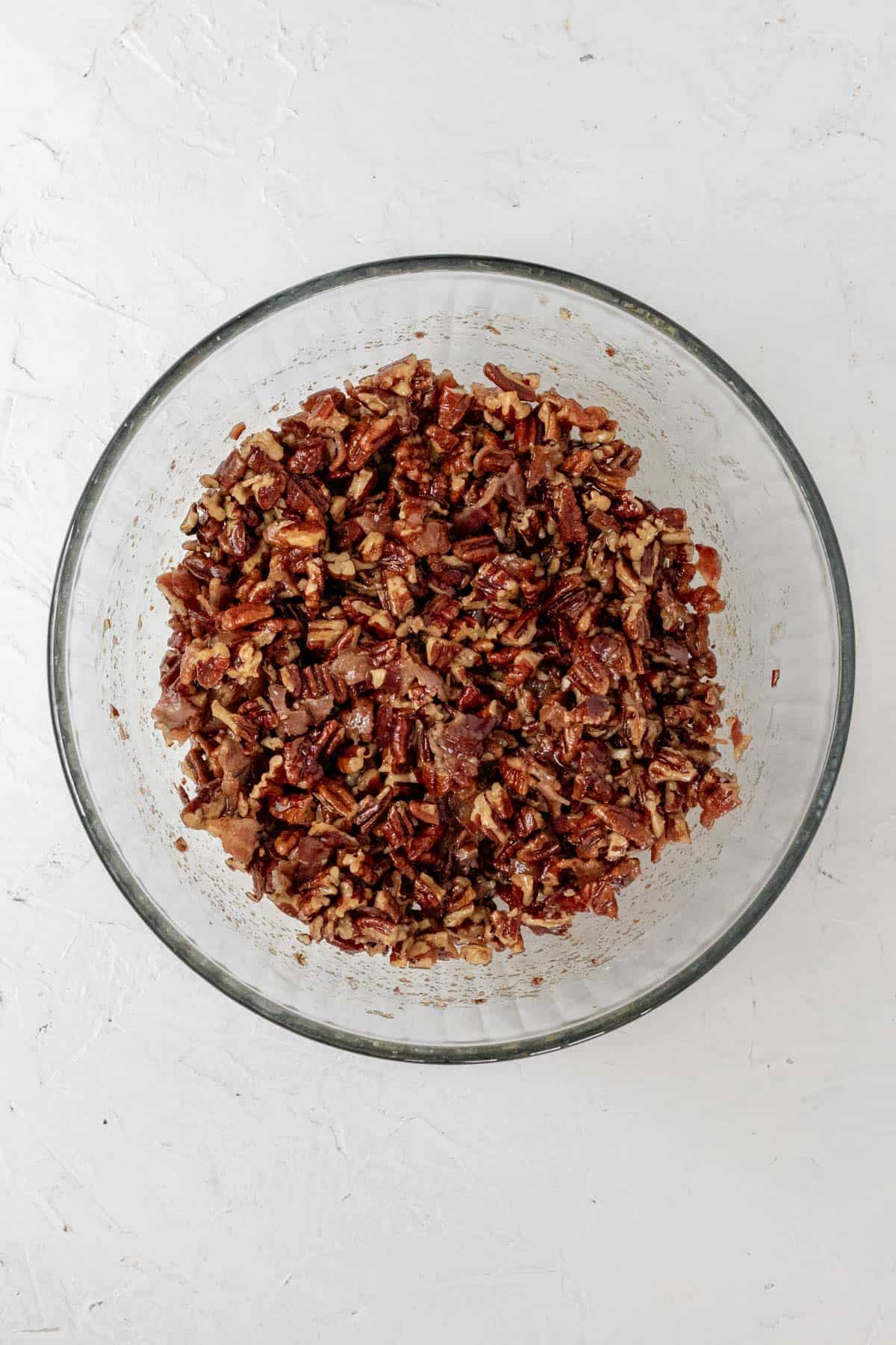 A mixture of bourbon, bacon, pecans, brown sugar, and melted better in a large glass mixing bowl.