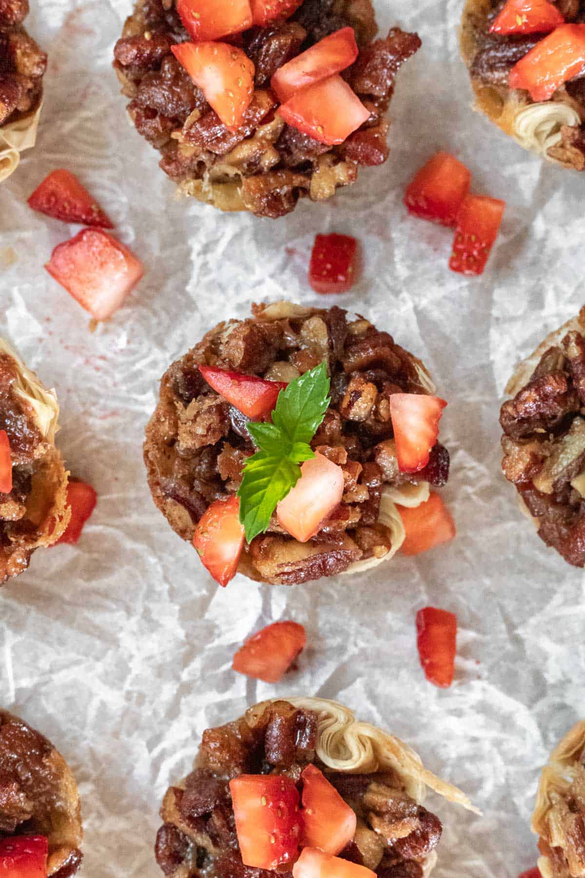 An overhead view of the bourbon pecan brie bites with diced strawberries scattered around and a garnish of mint.