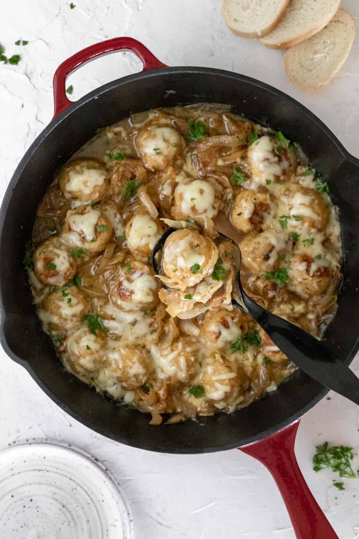 French onion chicken meatballs topped with melted gruyere cheese in a cast iron skillet.