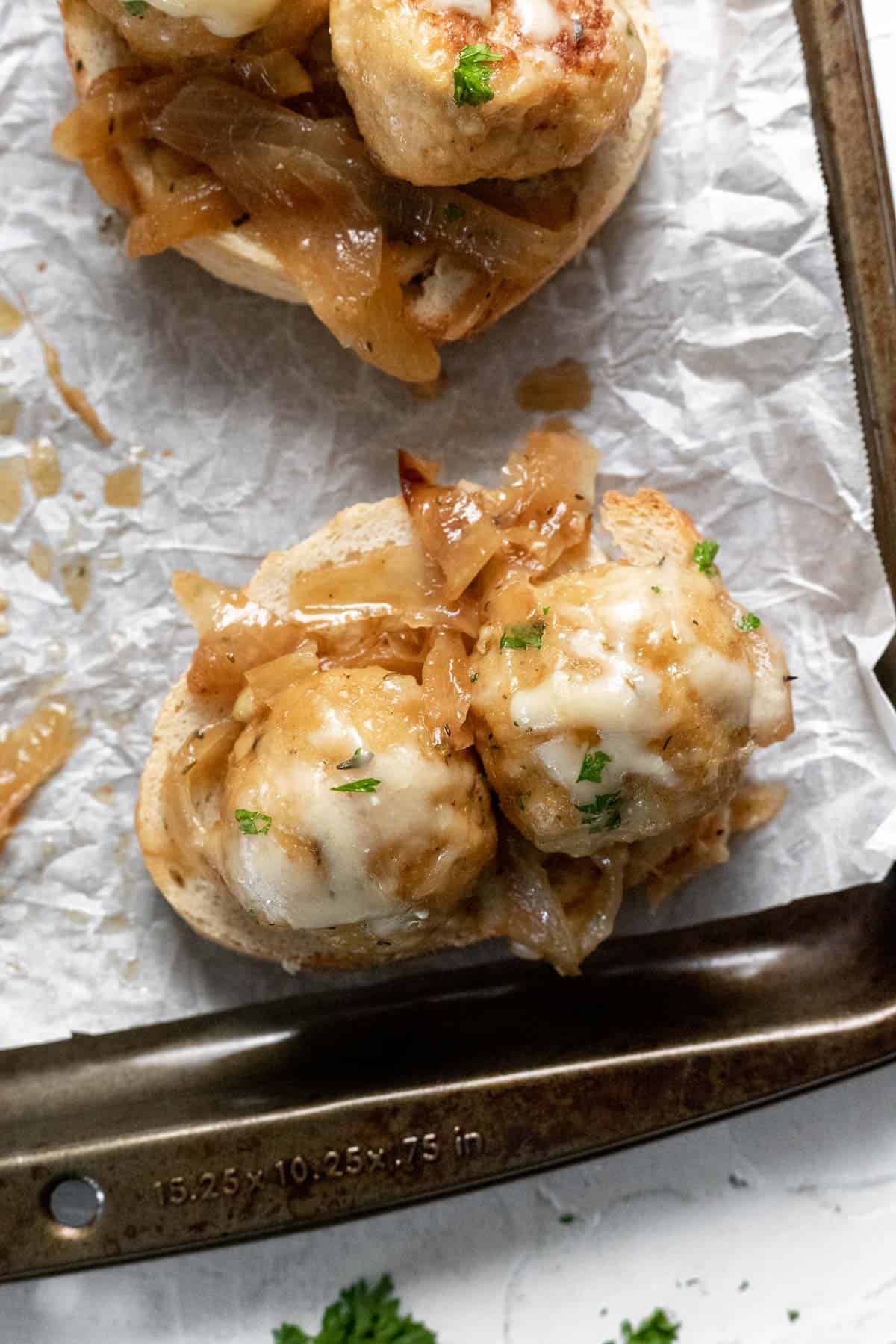 2 cheesy french onion chicken meatballs on a slice of toasted bread with caramelized onions around it.