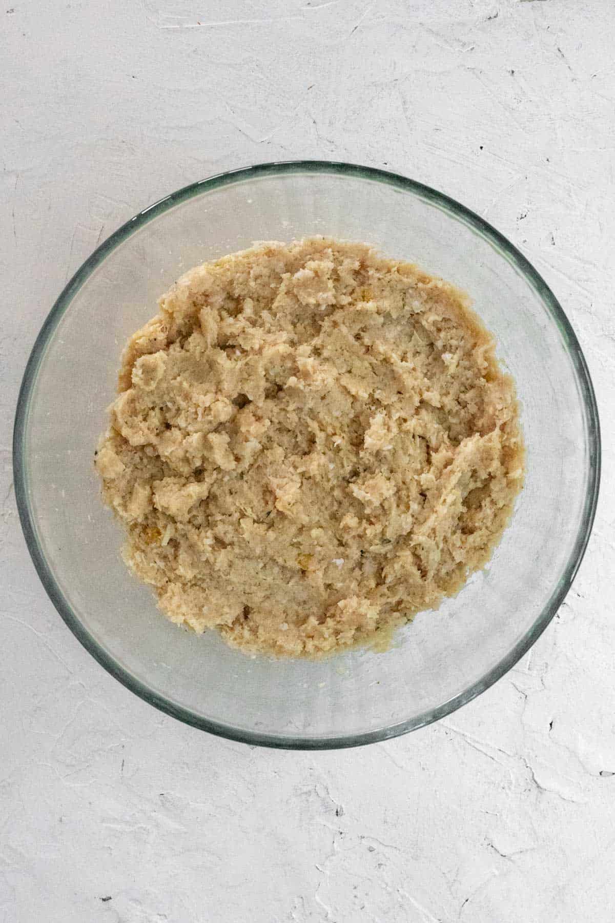 Raw ground chicken mixed with the other meatball ingredients in a glass bowl.