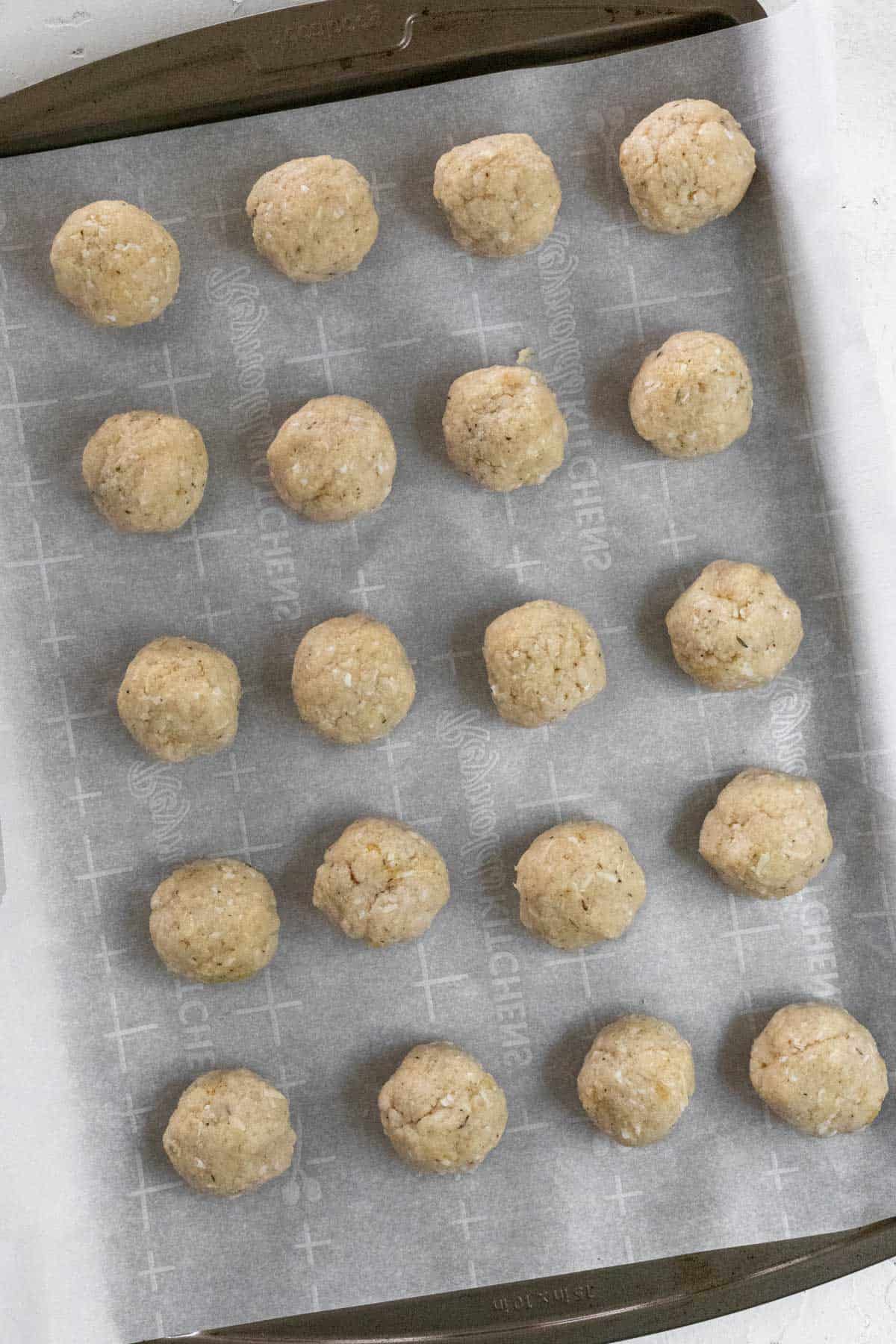 Raw meatball mixture formed into meatballs and lined up on a sheet pan.