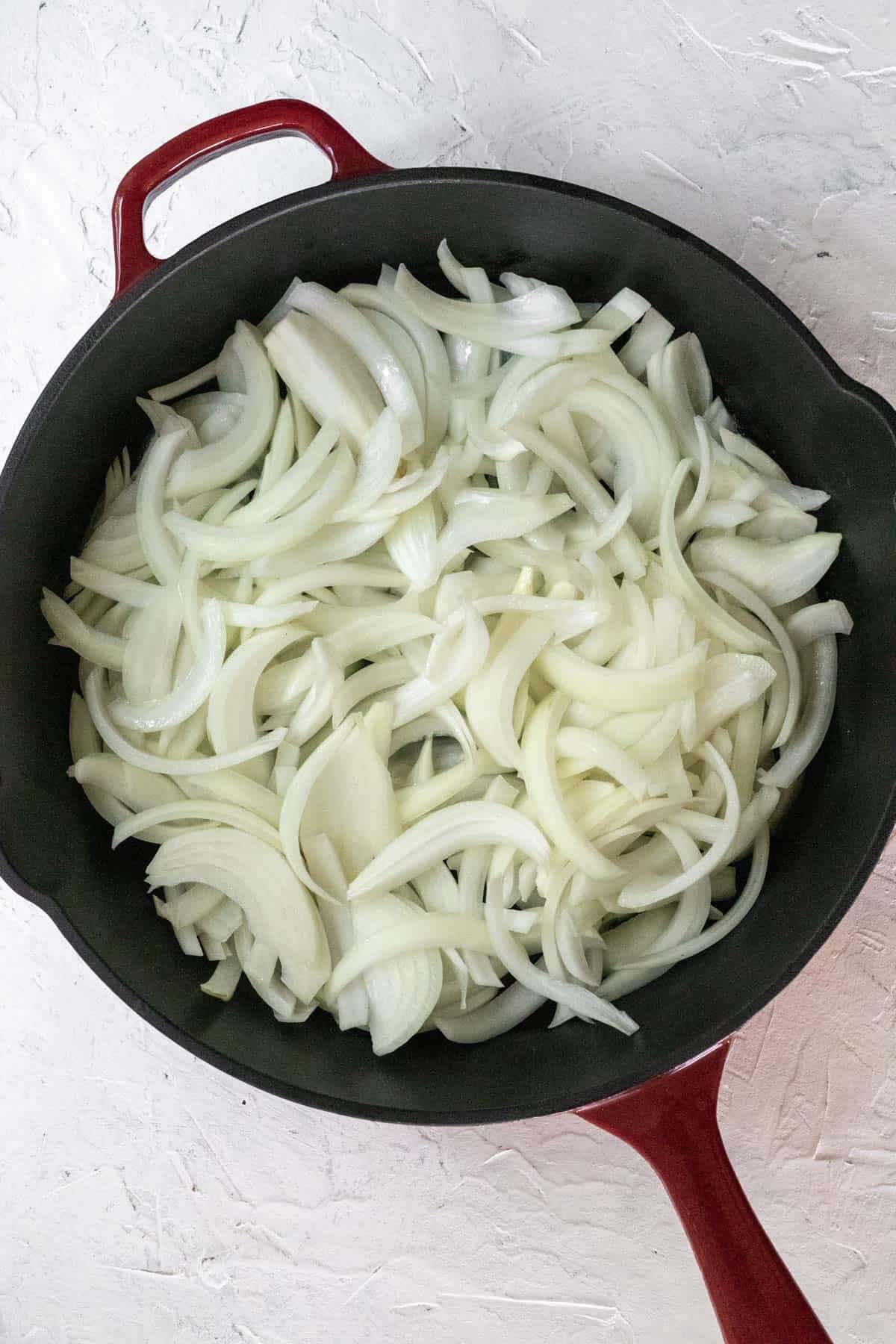 Raw sliced onions in a cast iron skillet before caramelizing.