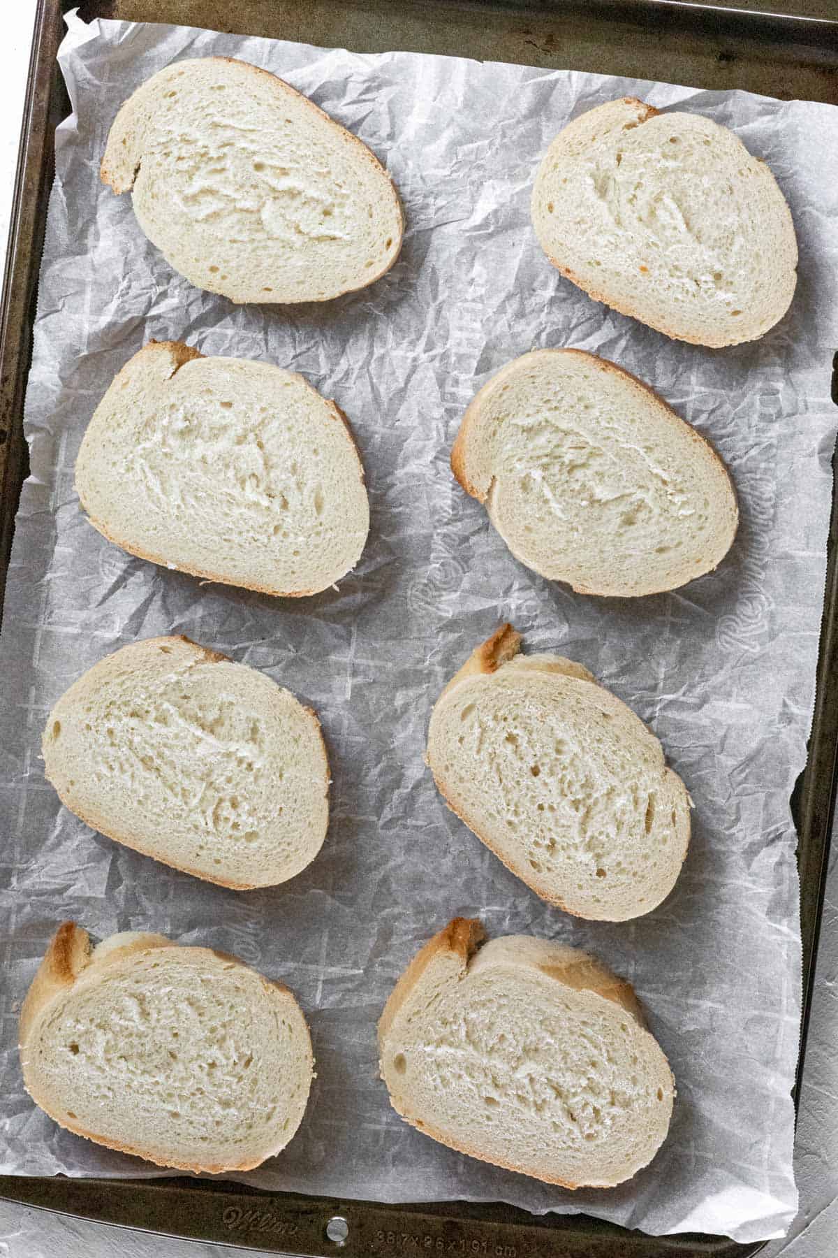 Sliced french bread lined up on a sheet pan before toasting.