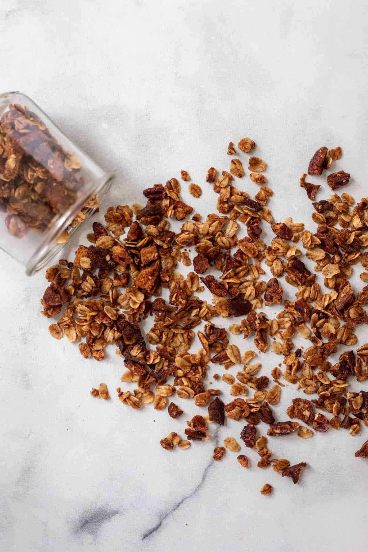 Baked granola spread spilled from a jar and spilled out across a white backdrop.