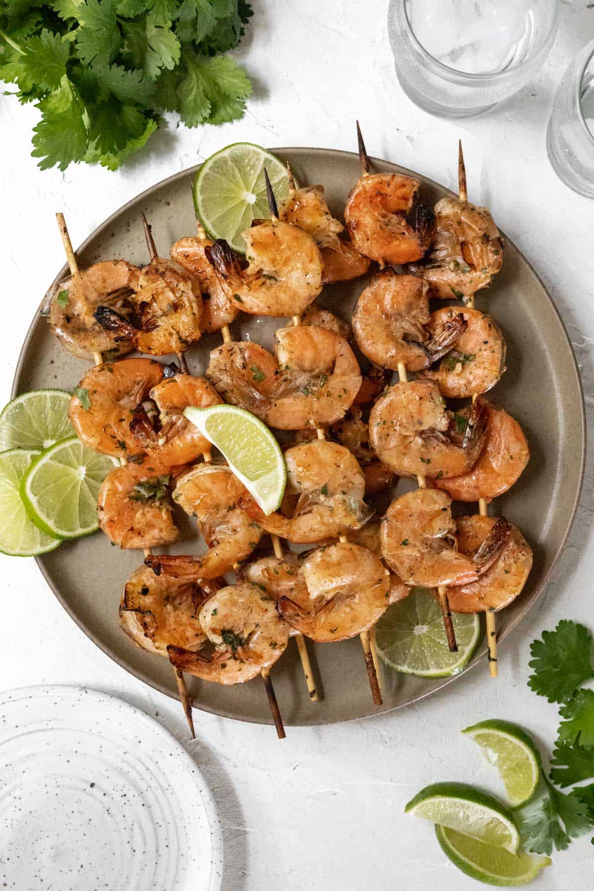 Grilled shrimp skewers garnished with limes on a beige plate.