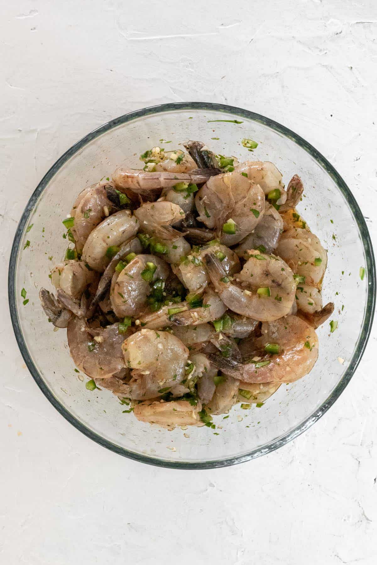 Raw shrimp mixed with the tequila lime marinade in a glass bowl.