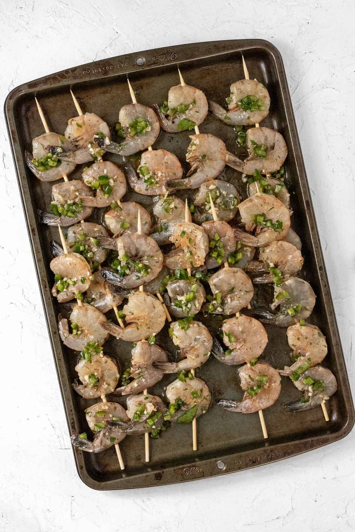 Raw marinated shrimp on skewers on a sheet pan.