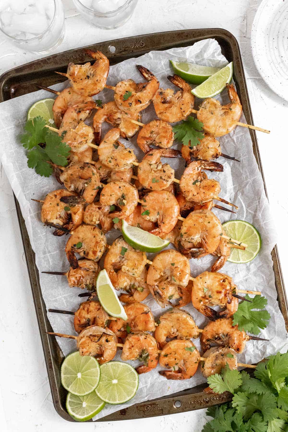 Grilled margarita shrimp skewers on a sheet pan with limes and cilantro.