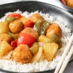 Sweet and sour chicken meatballs with stir fried peppers, onions, and pineapple on a bed of white rice.