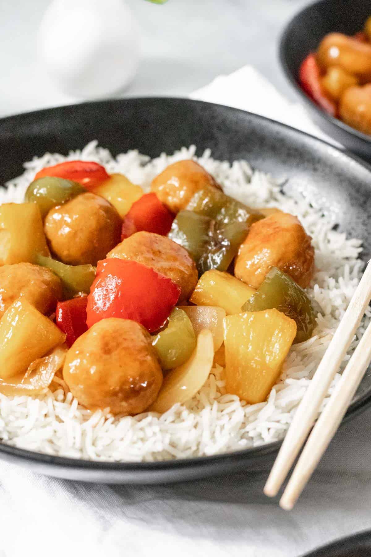 Sweet and sour chicken meatballs with stir fried peppers, onions, and pineapple on a bed of white rice.