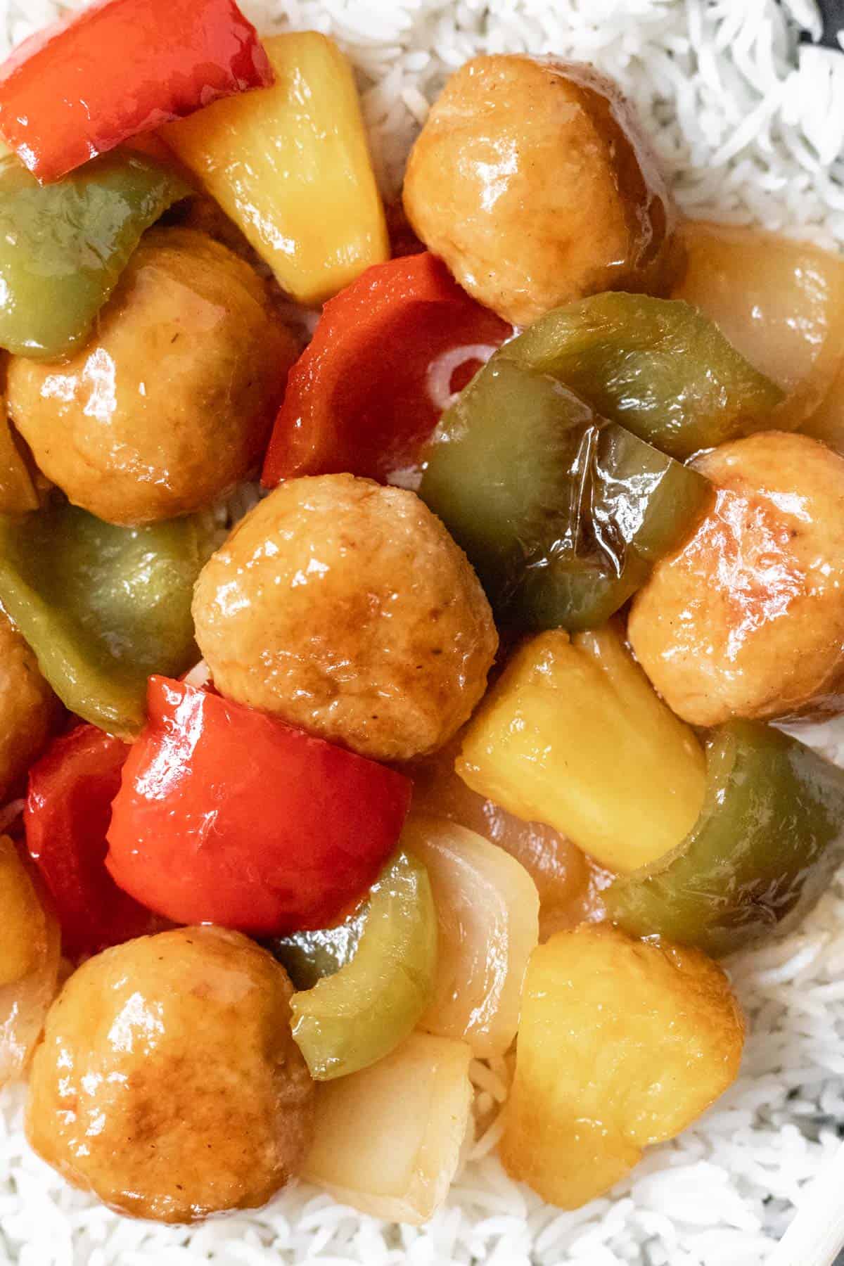 A closeup of meatballs, peppers, pineapple, and onions glazed with sweet and sour sauce.