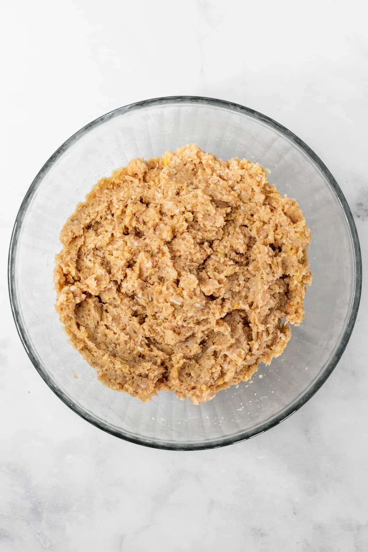 Ground chicken mixed with the other meatball ingredients in a large glass bowl.