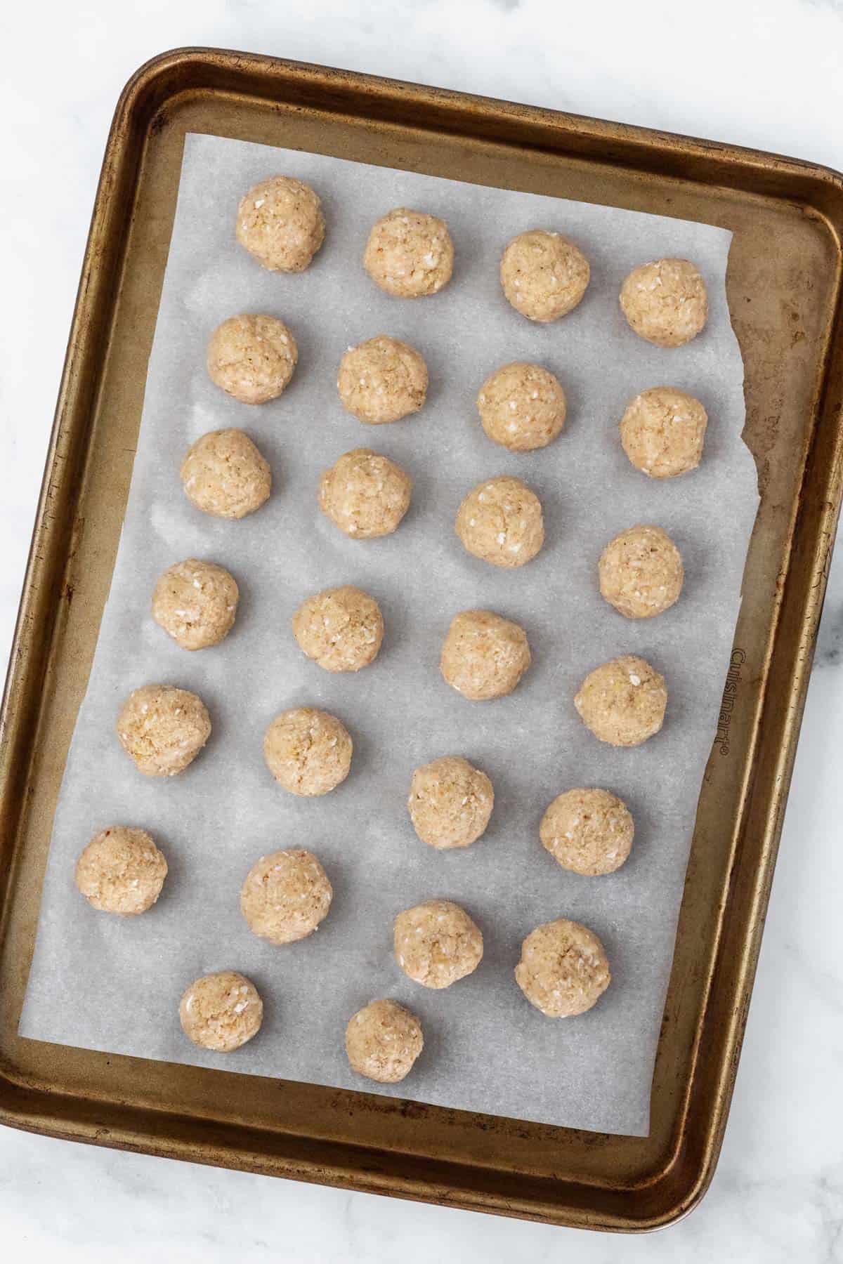 Raw meatballs shaped on a baking sheet lined with parchment paper before being placed in the oven.