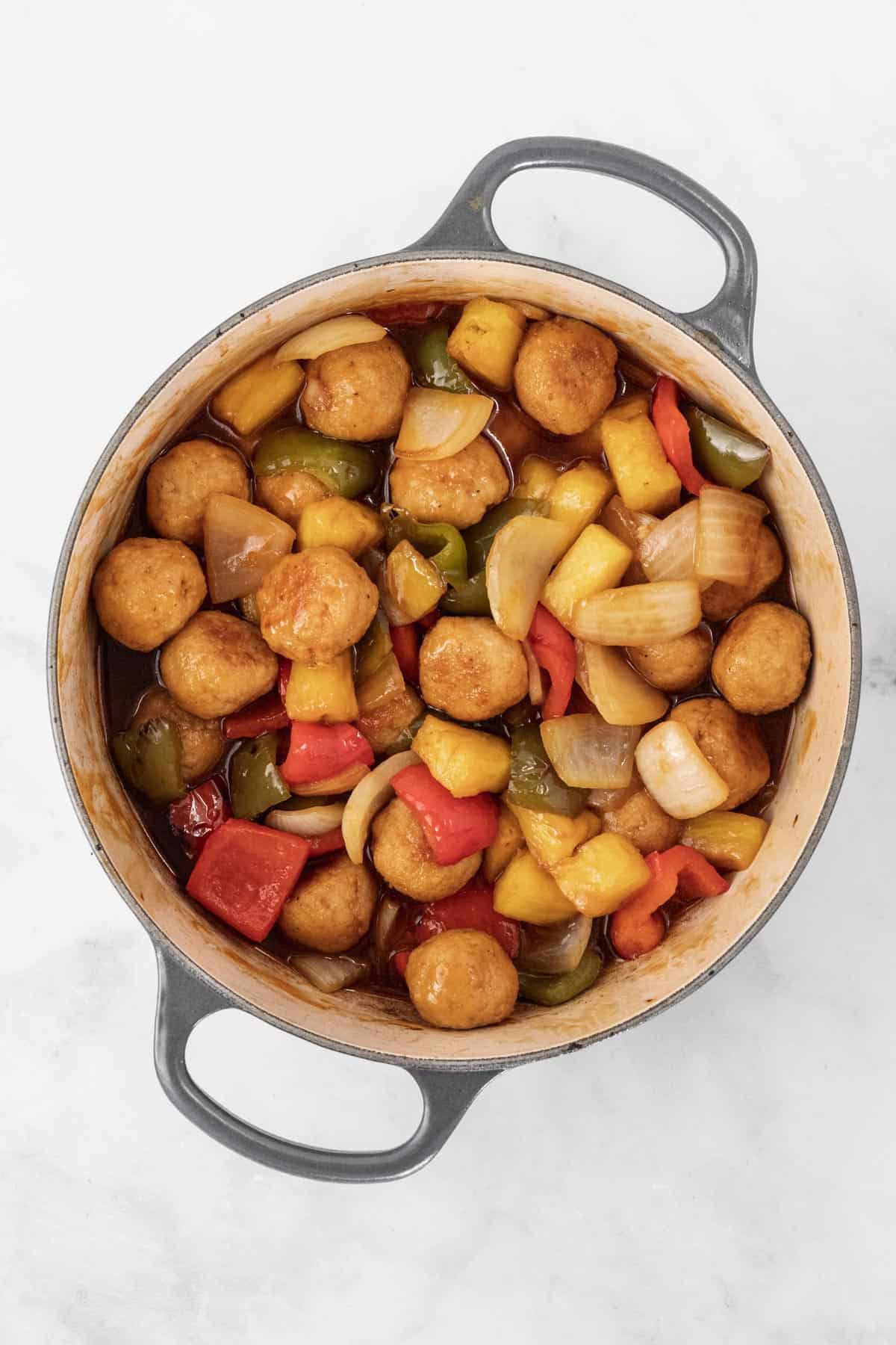 Baked meatballs, stir fried vegetables, pineapple, and sweet and sour sauce mixed together in a dutch oven.