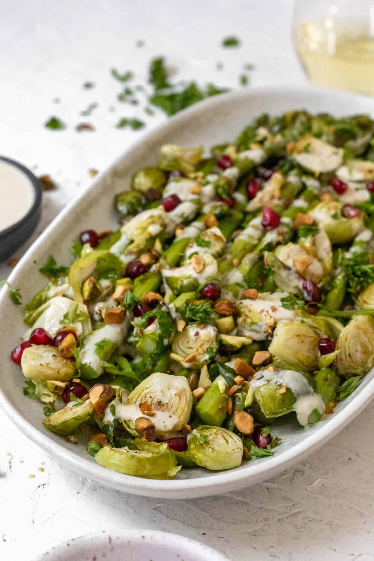 Side view of asparagus, brussels sprouts, lemon tahini sauce, pistachios, and pomegranate seeds on an oval platter.