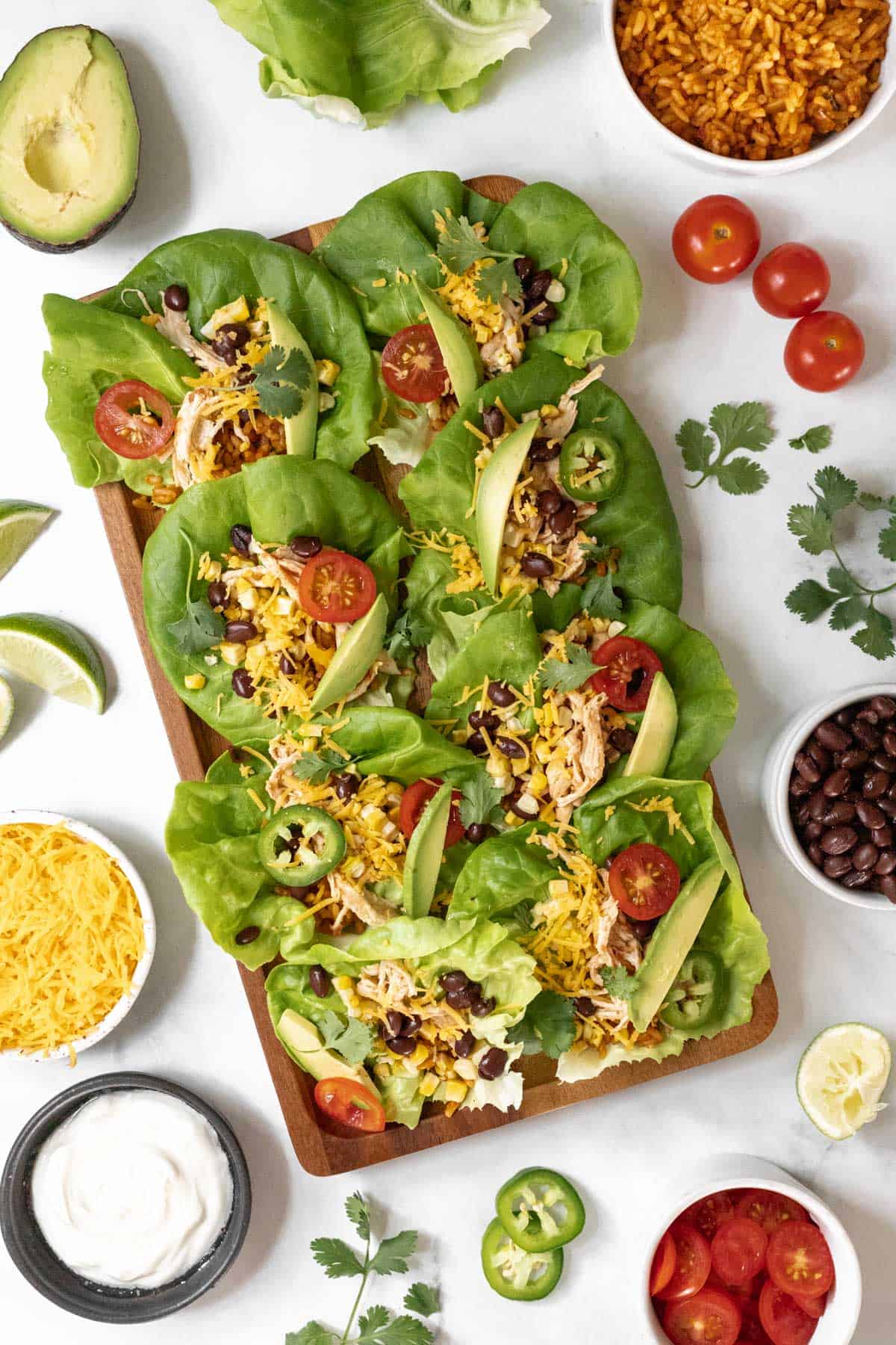 Overhead view of shredded chicken lettuce wraps on a rectangular serving platter with the taco fixings around it.