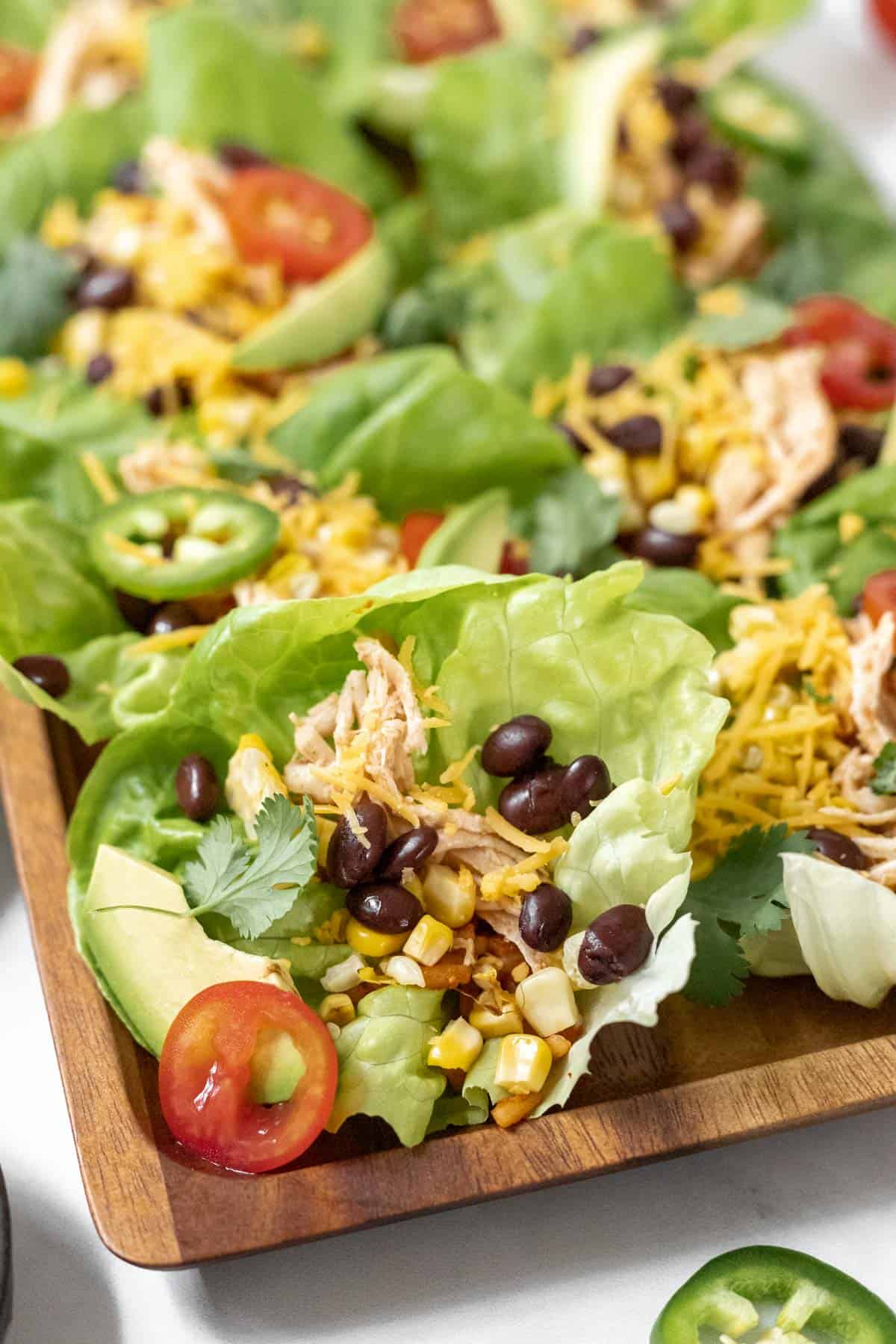 A closeup look at all the fixings inside a lettuce wrap taco: beans, corn, avocado, tomatoes, and shredded chicken.