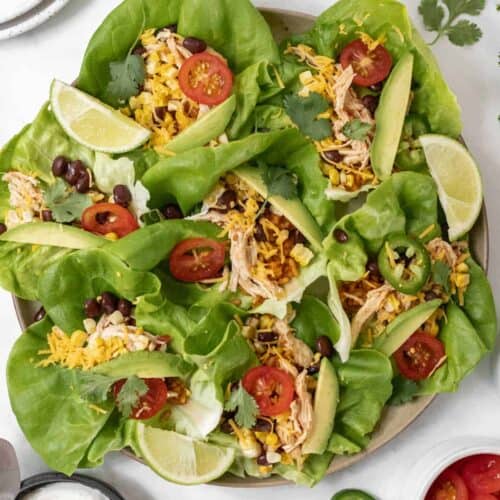 Shredded chicken taco lettuce wraps on a round platter with all the fixings around it.