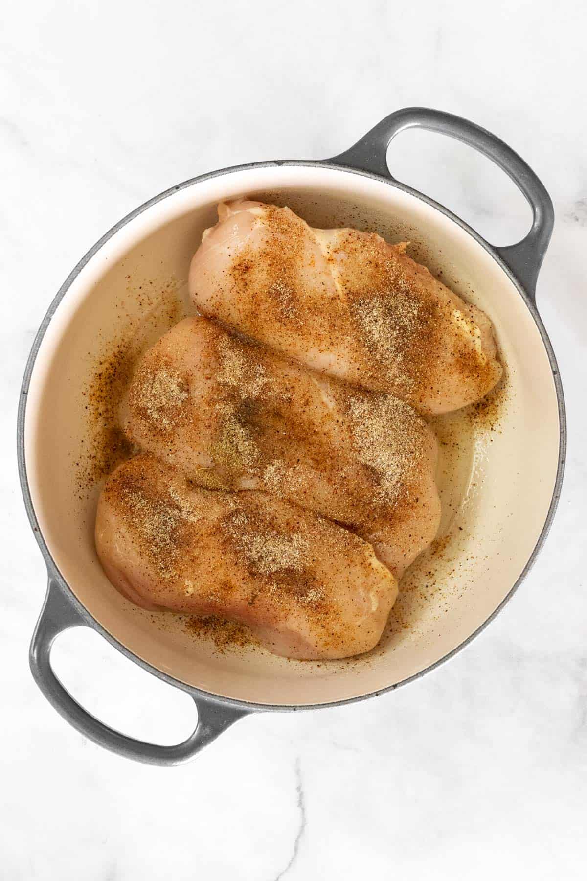 Raw chicken breasts seasoned in a dutch oven.