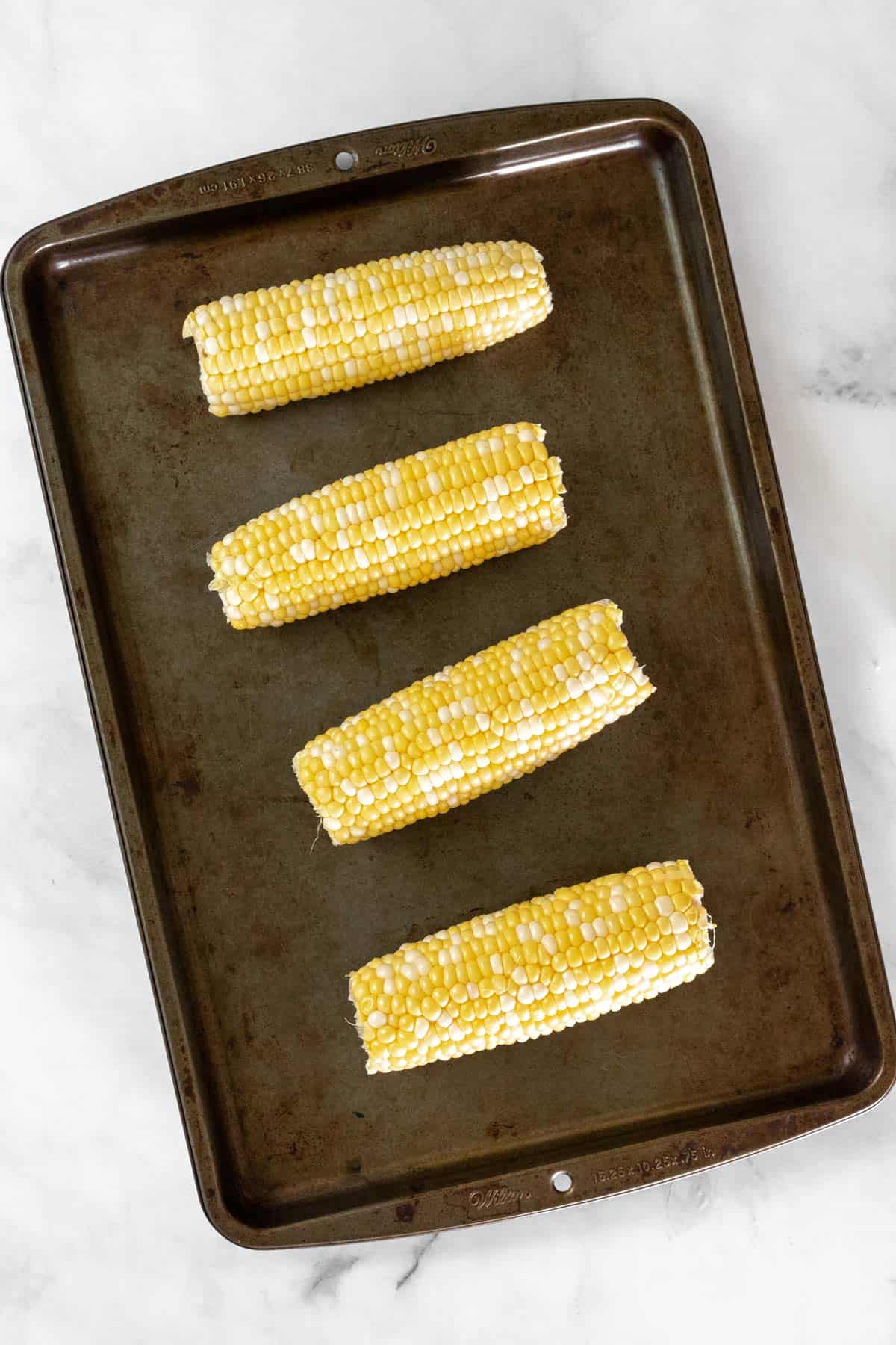 Uncooked corn on the cob on a sheet pan.