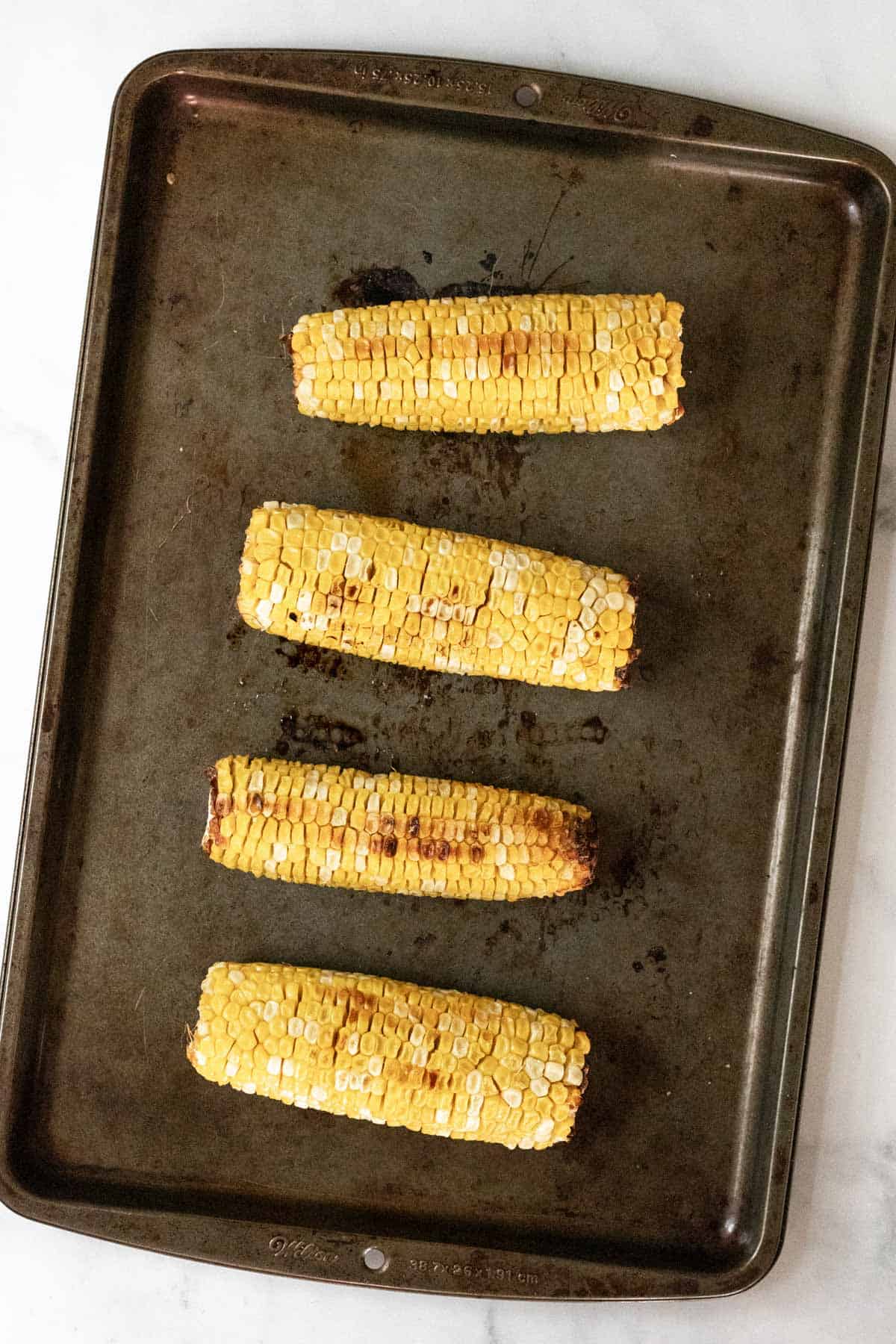 4 roasted corn on the cobs on a sheet pan.