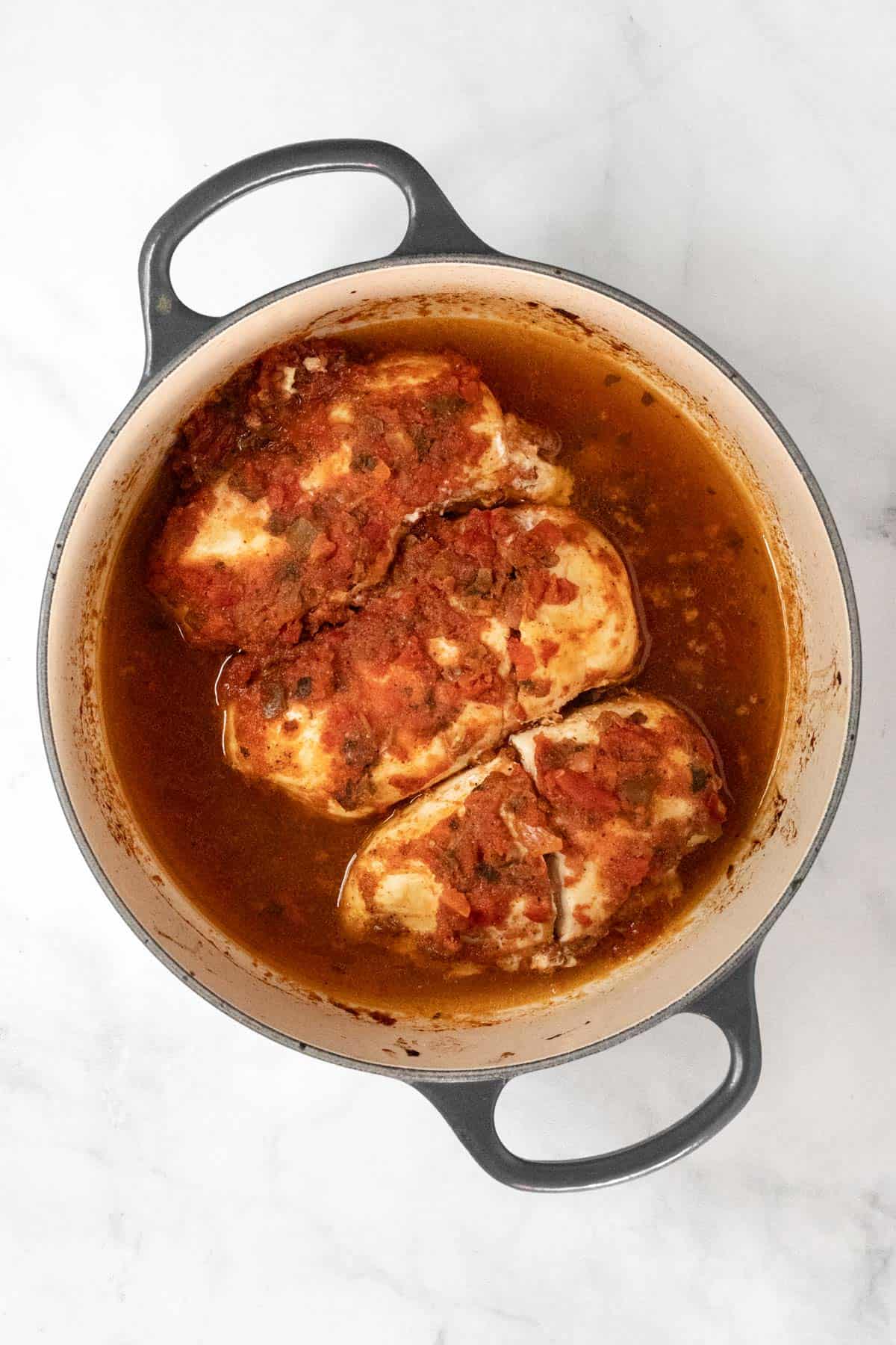 Cooked chicken breasts topped with salsa in a dutch oven.