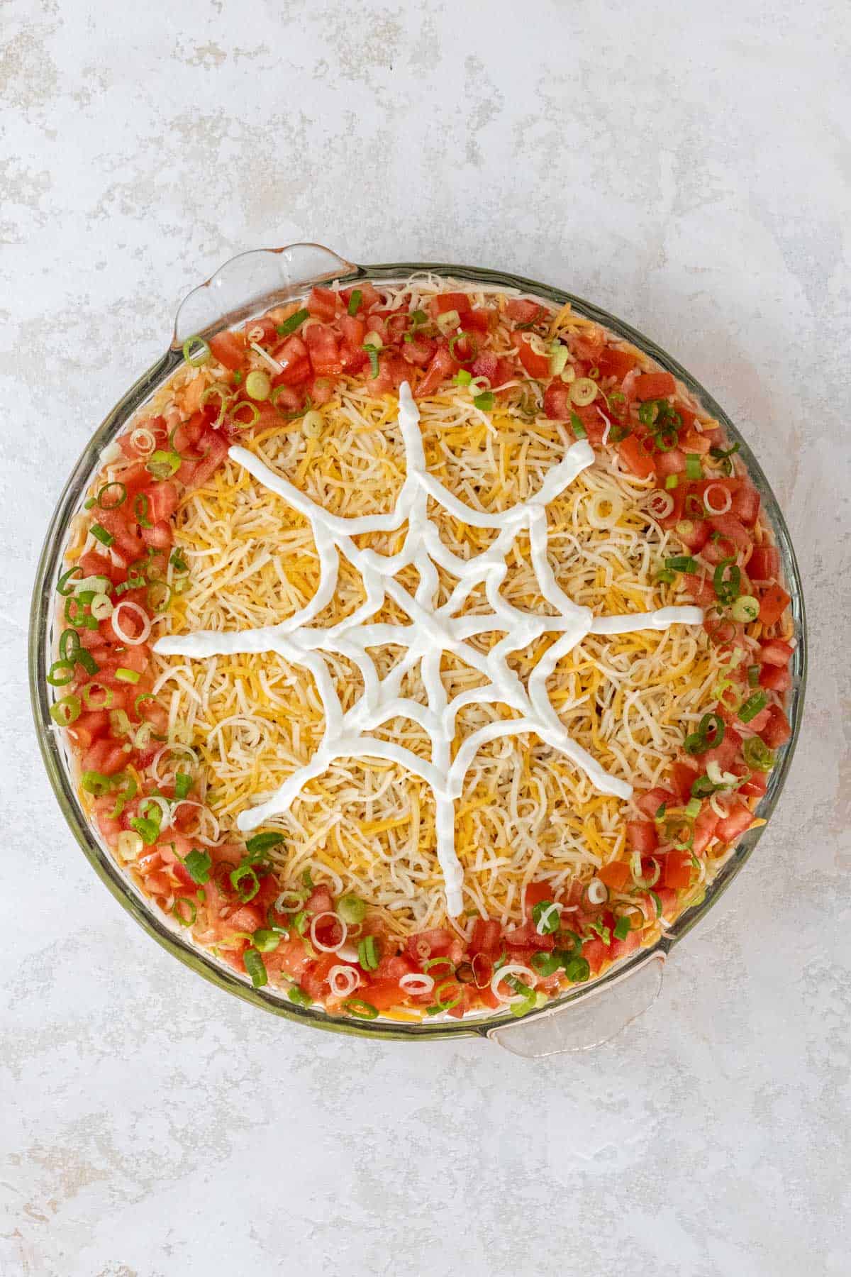 A sour cream spiderweb in progress on top of the shredded cheese.