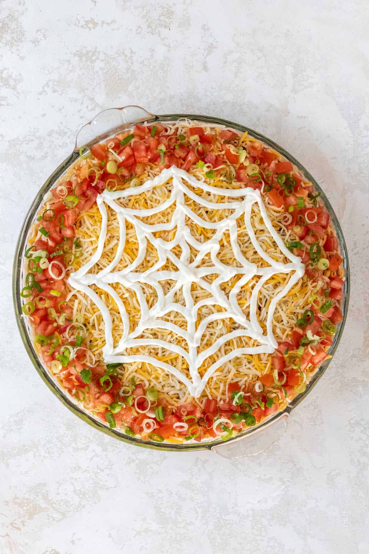 A completed sour cream spiderweb on top of the shredded cheese.