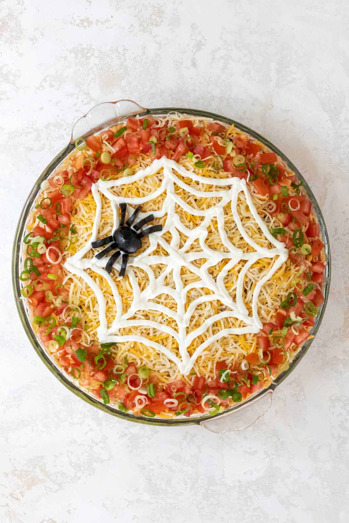 A completed Halloween 7 layer taco dip with a black olive spider on top of the sour cream spiderweb.