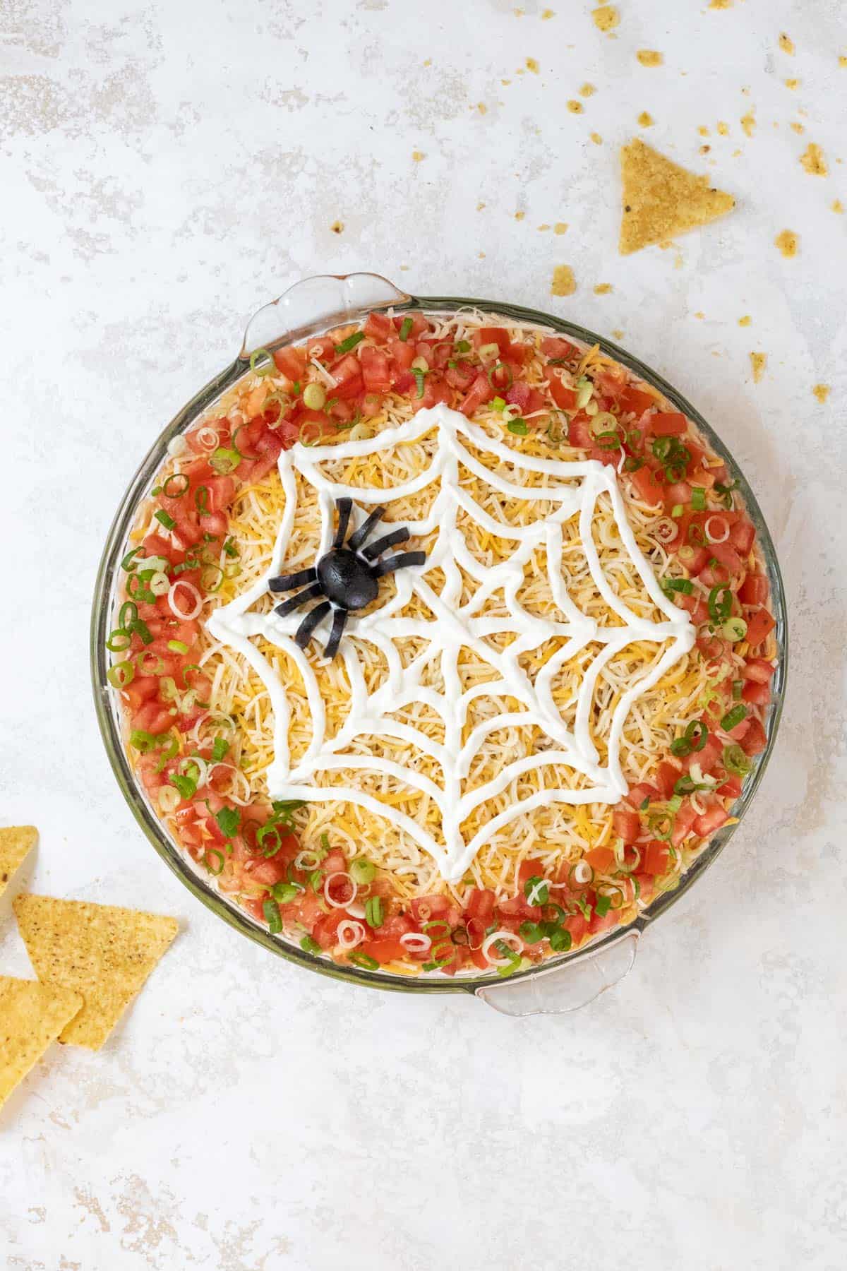 A completed Halloween 7 layer taco dip with a black olive spider on top of the sour cream spiderweb.