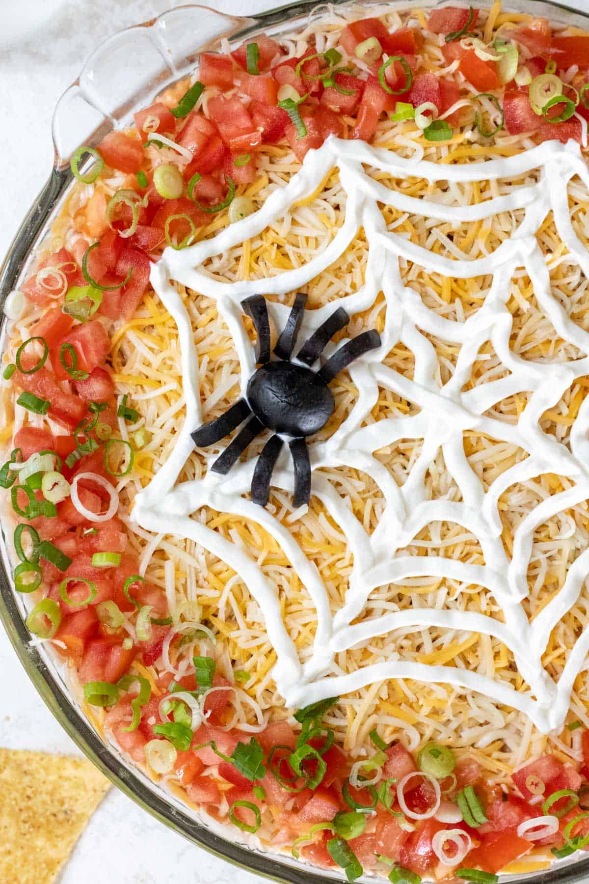 A closeup of a spider made out of black olives and a web made out of sour cream on top of Halloween taco dip.