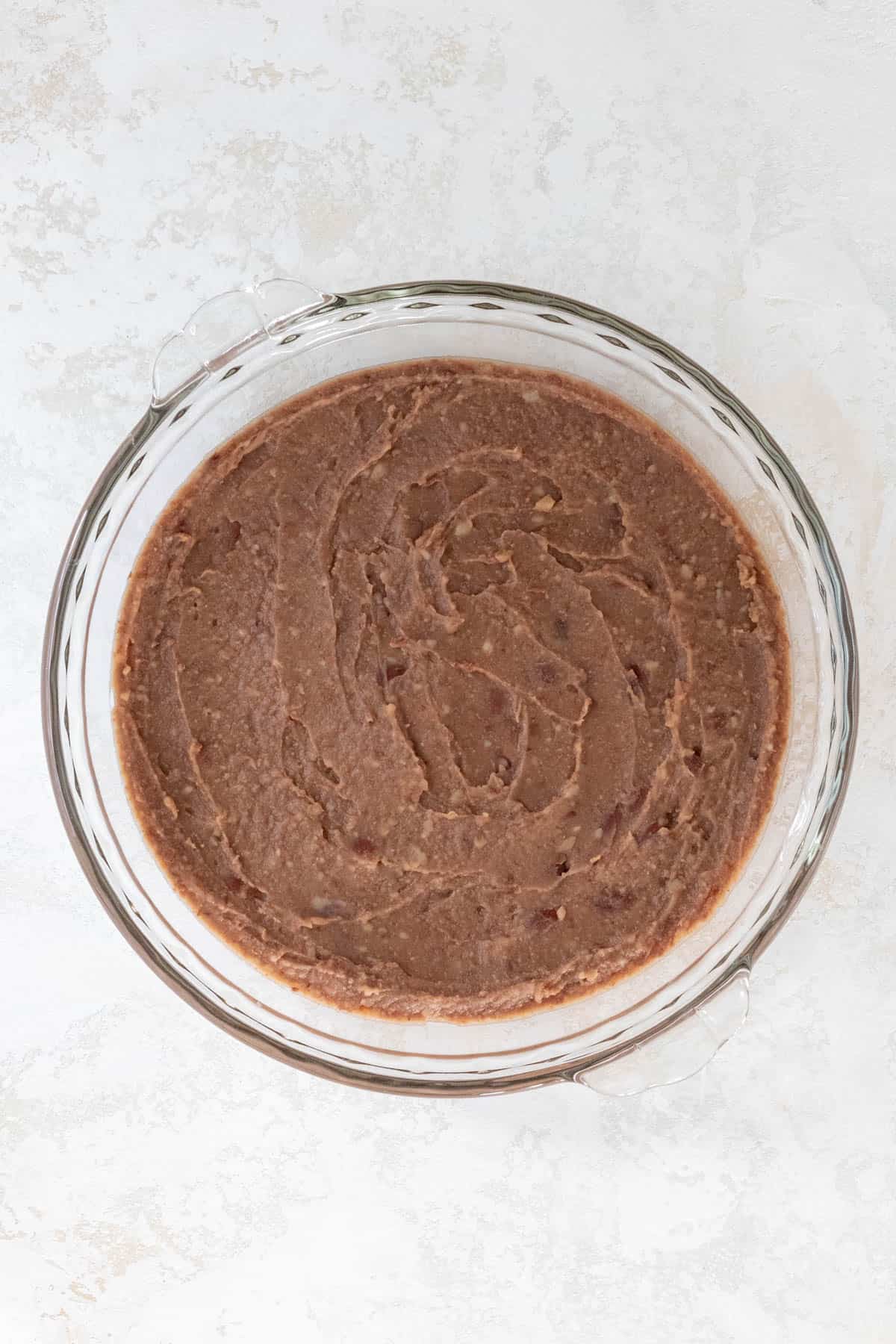 Refried beans spread out in a large pie dish.