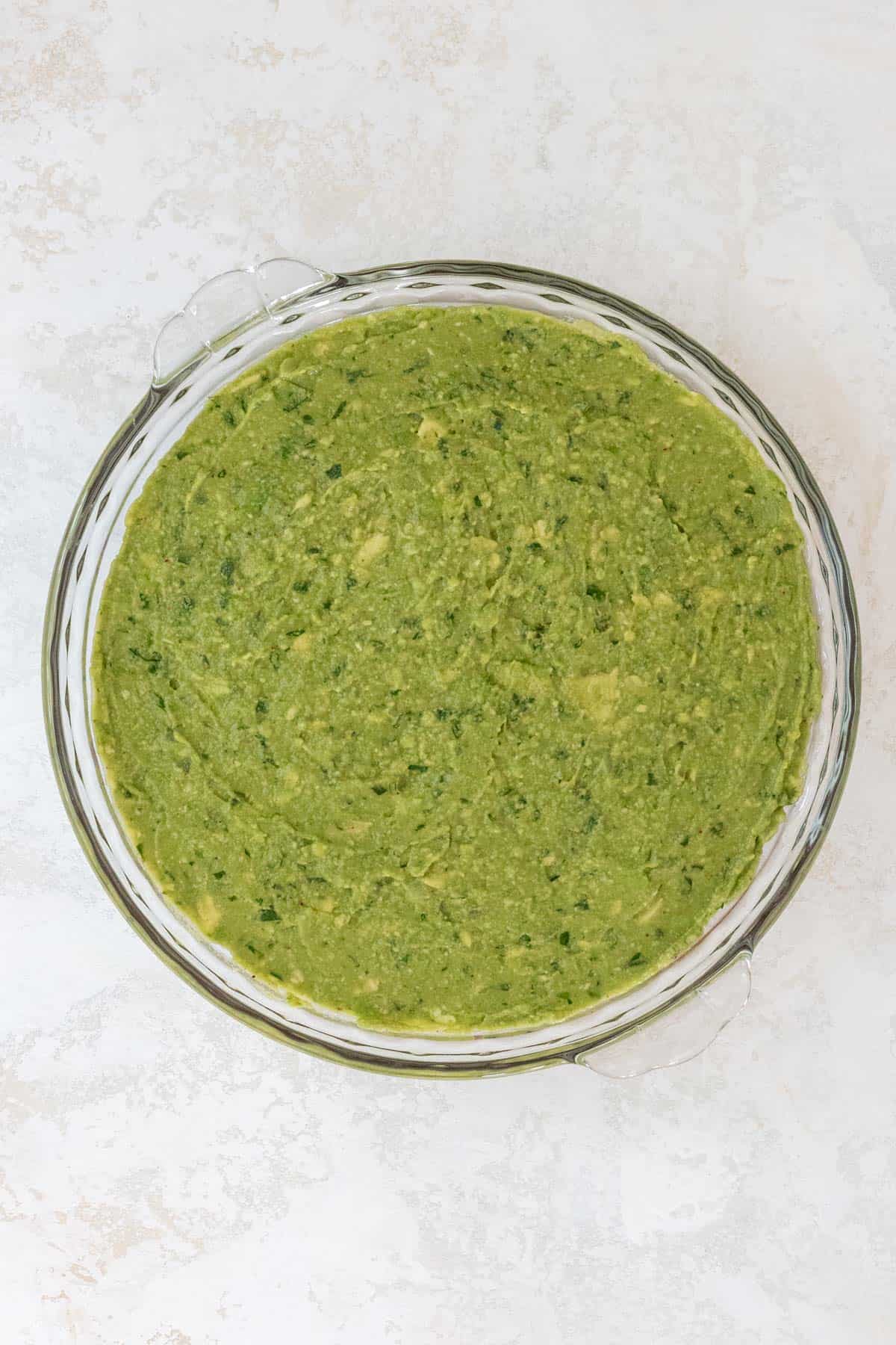 Homemade guacamole spread out on top of the refried beans in a large pie dish.