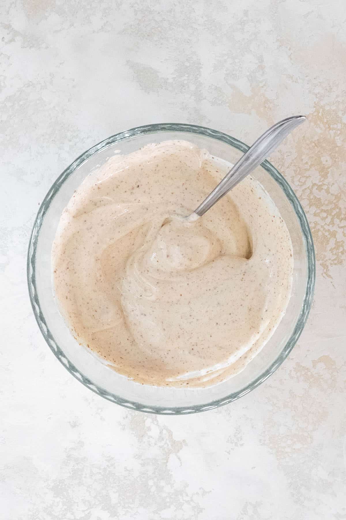 Sour cream mixed with spices in a glass mixing bowl.