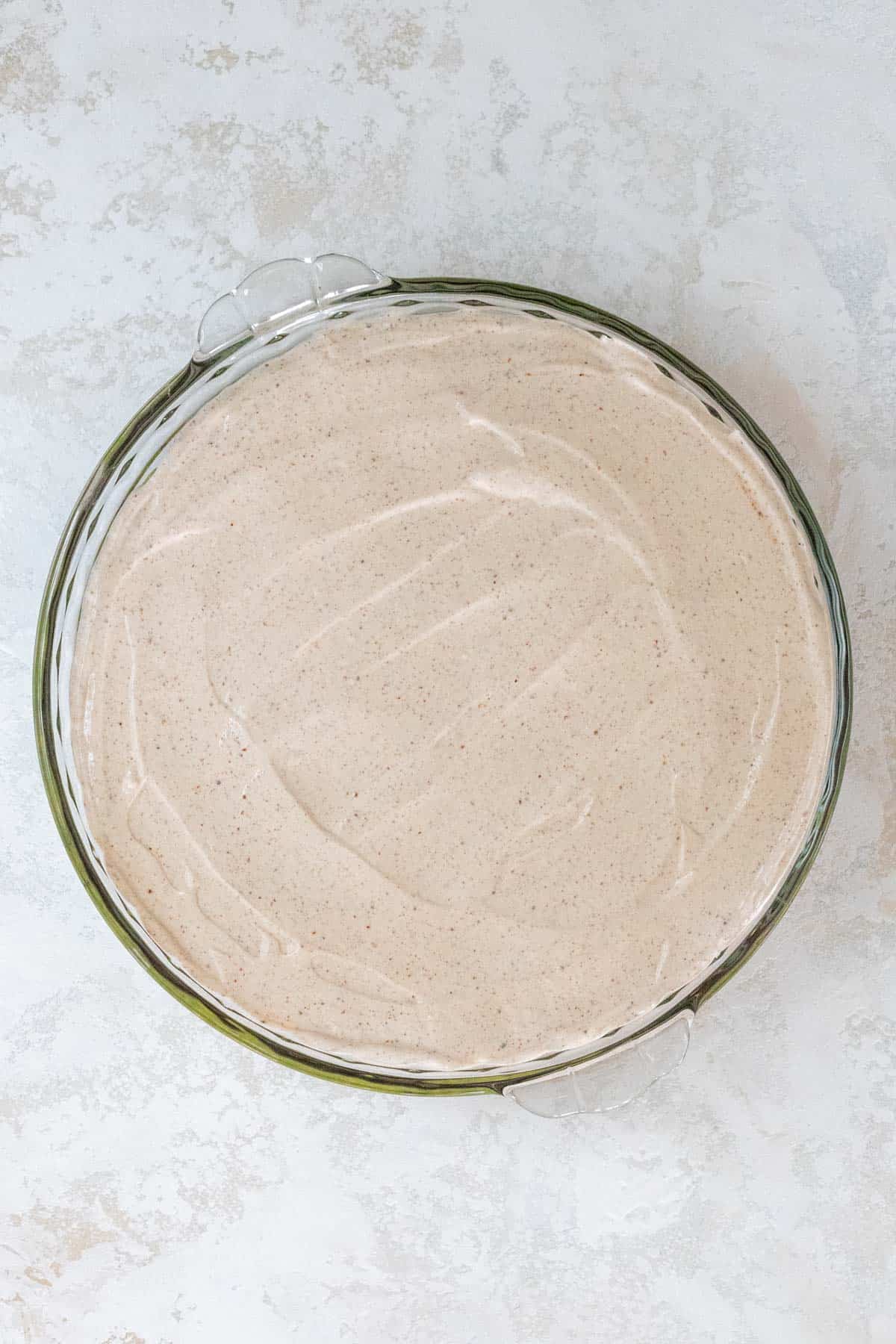 Sour cream mixed with spices spread out on top of guacamole in a large pie dish.